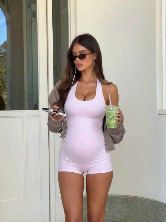 A stylish pregnant woman in a pink bodysuit holding a green smoothie, representing EasyLean's commitment to home fitness for moms and postpartum recovery.