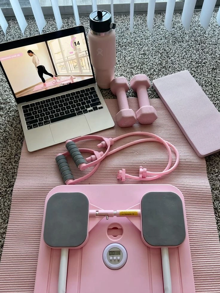 Pink EasyLean home fitness starter kit featuring a foldable pilates reformer, dumbbells, resistance bands, and a yoga mat next to a laptop showing a workout tutorial.