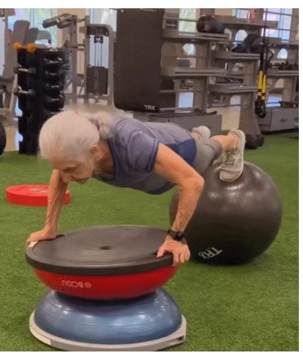 An elderly senior woman performing a high-level plank on a BOSU ball and stability ball to demonstrate peak functional fitness and physical longevity
