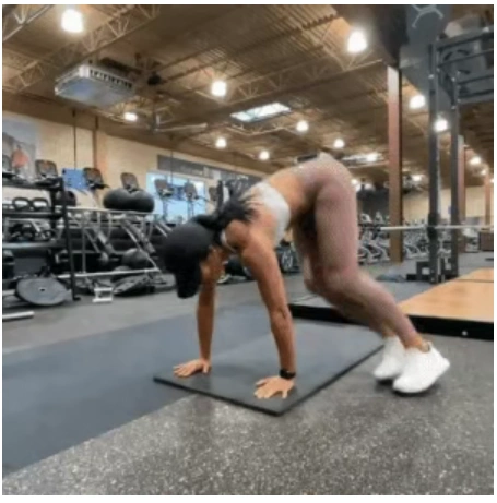 A fit woman in a white sports bra and dark cap performing a plank with lateral tuck jump on a black mat to break a home fitness plateau