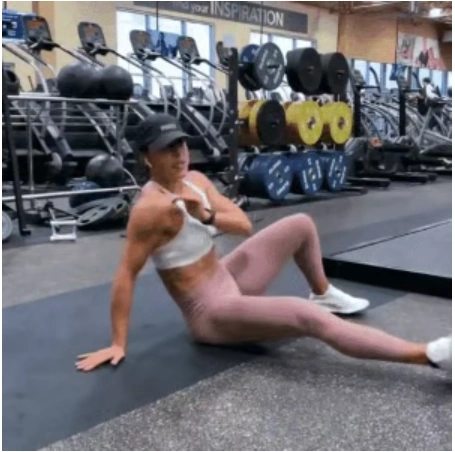 A fit woman in a white sports bra and pink leggings performing a plank with torso rotation and kick on a black mat to break a fitness plateau