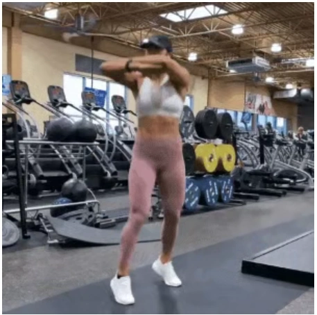 A fit woman in a white sports bra and pink leggings performing a squat jump with hip rotation in the gym to break a home fitness plateau