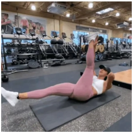 A fit woman in pink leggings performing a supine alternating leg lift with hand-to-foot touch on a fitness mat to break a home workout fitness plateau